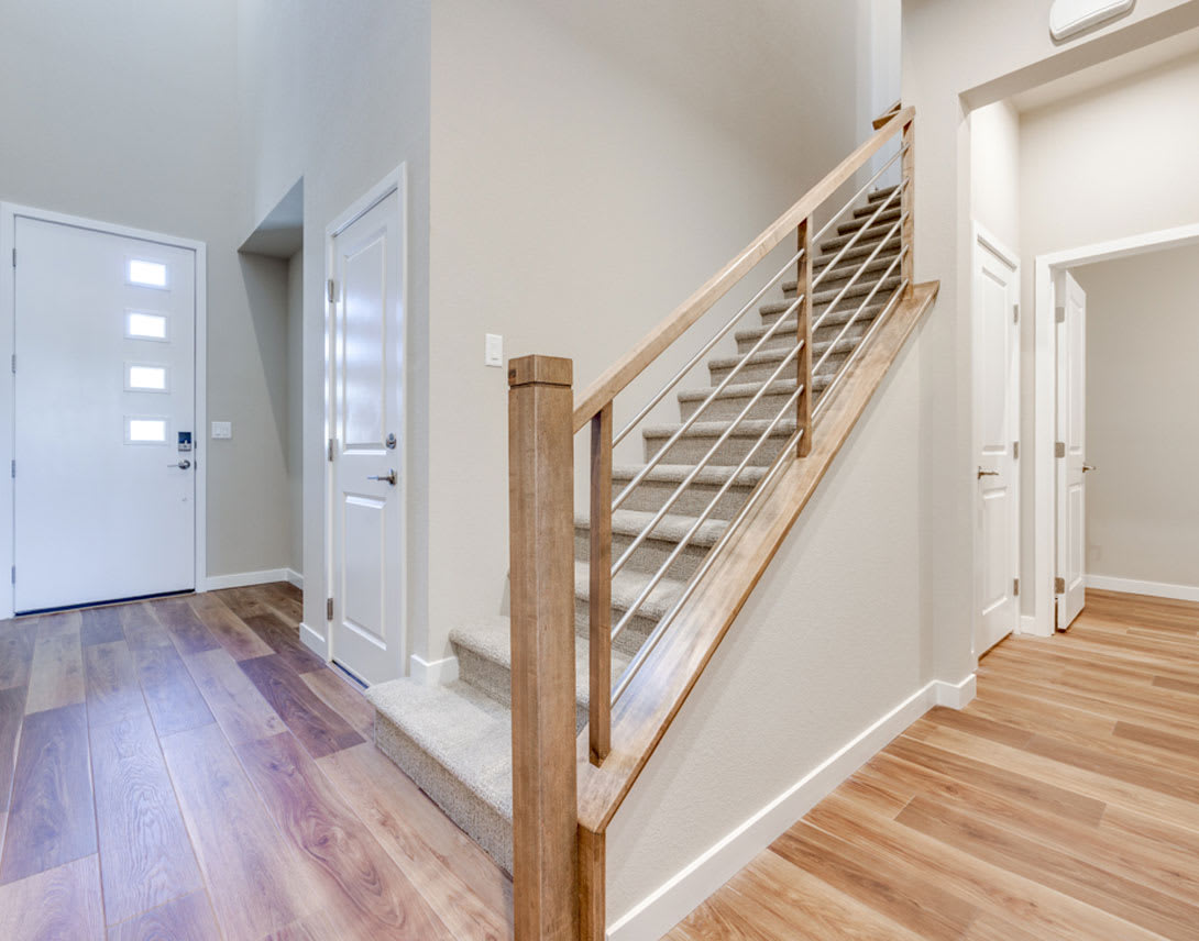 A bright and spacious hallway with a wooden staircase and railing, leading to various rooms with white walls and hardwood floors.