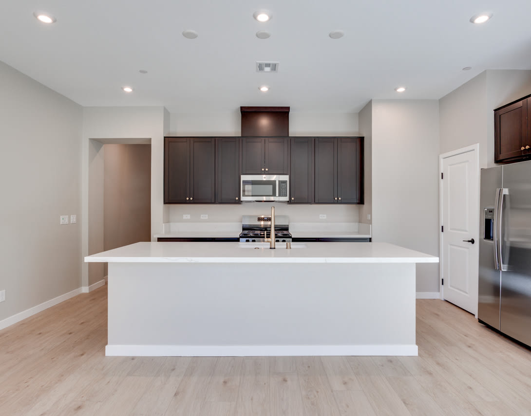 A modern, open-concept kitchen with dark wood cabinets, a white island countertop, and hardwood flooring.