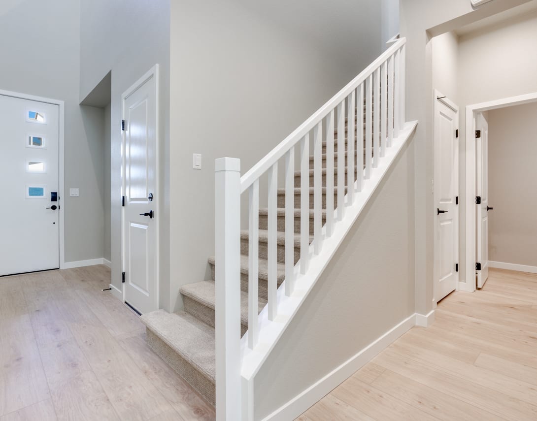 A bright and airy hallway with a white staircase and railing, leading to several doors and a hardwood floor.