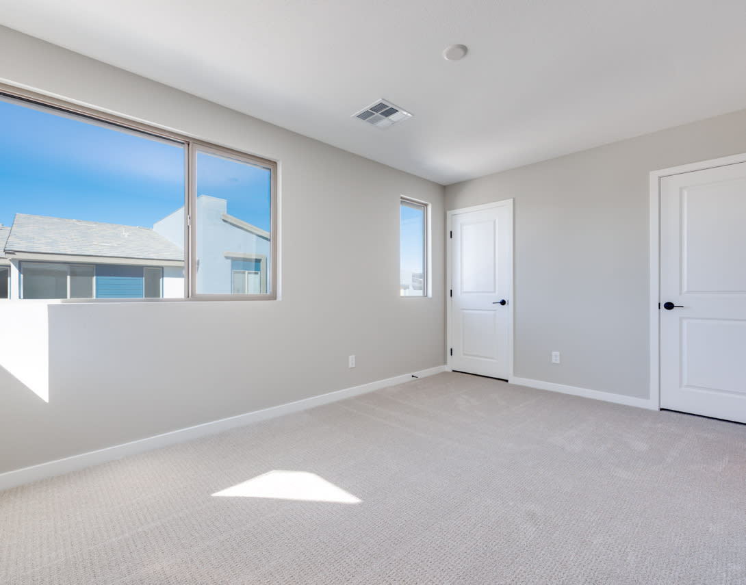 A spacious, well-lit room with white walls, a carpeted floor, and a large window overlooking a residential neighborhood.