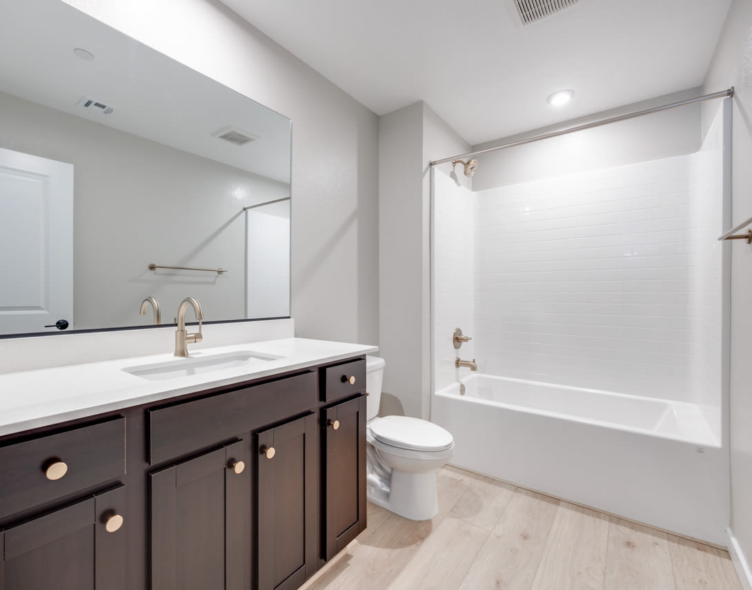 A modern bathroom with a dark wood vanity, white countertop, and a bathtub against the wall.