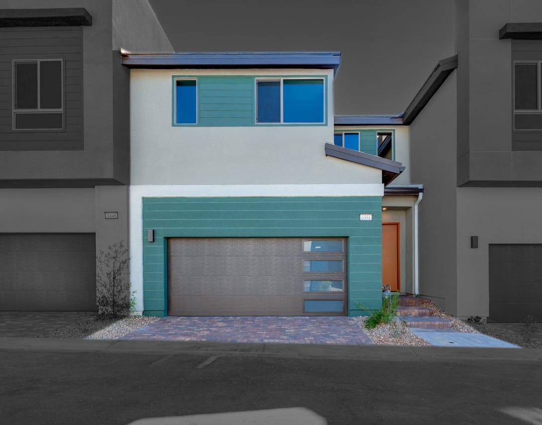 A modern, multi-colored townhouse with a garage door, surrounded by a paved driveway and landscaping.
