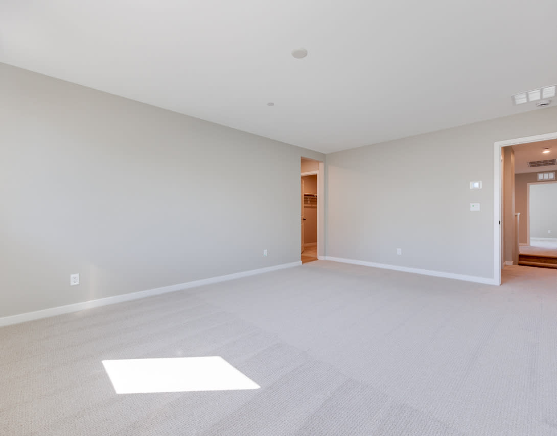 An empty, spacious room with light-colored walls, a wooden door frame, and a bright square of sunlight on the floor.