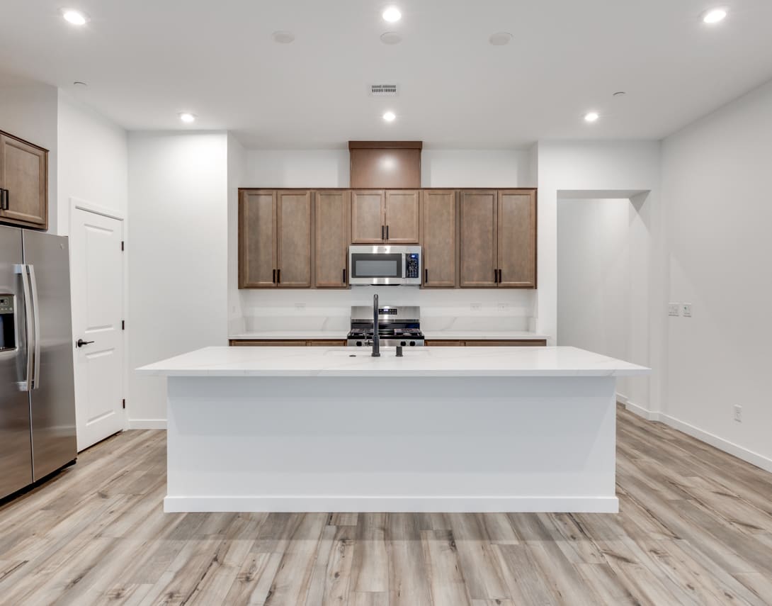 A modern, open-concept kitchen with white countertops, wooden cabinets, and stainless steel appliances, set against a backdrop of bright, well-lit space.