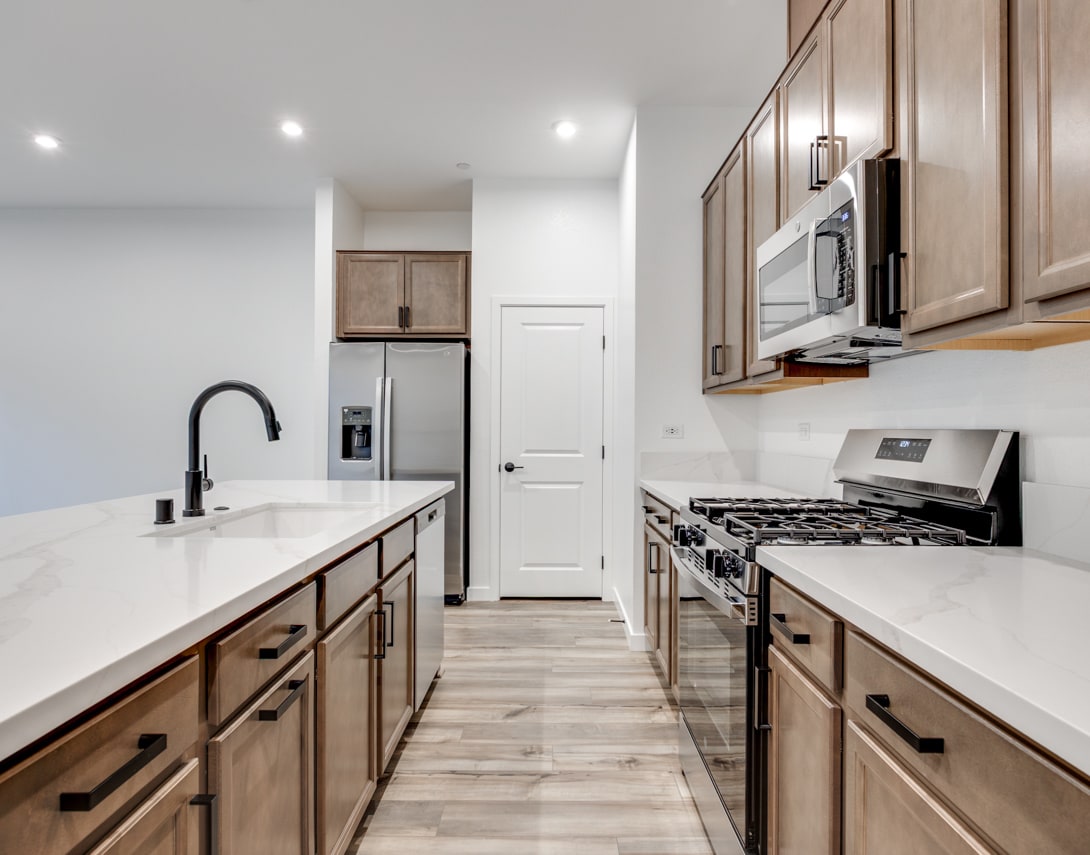 A modern, well-equipped kitchen with light-colored wood cabinets, white countertops, and stainless steel appliances, including a gas stove and a refrigerator, creating a clean and inviting atmosphere.