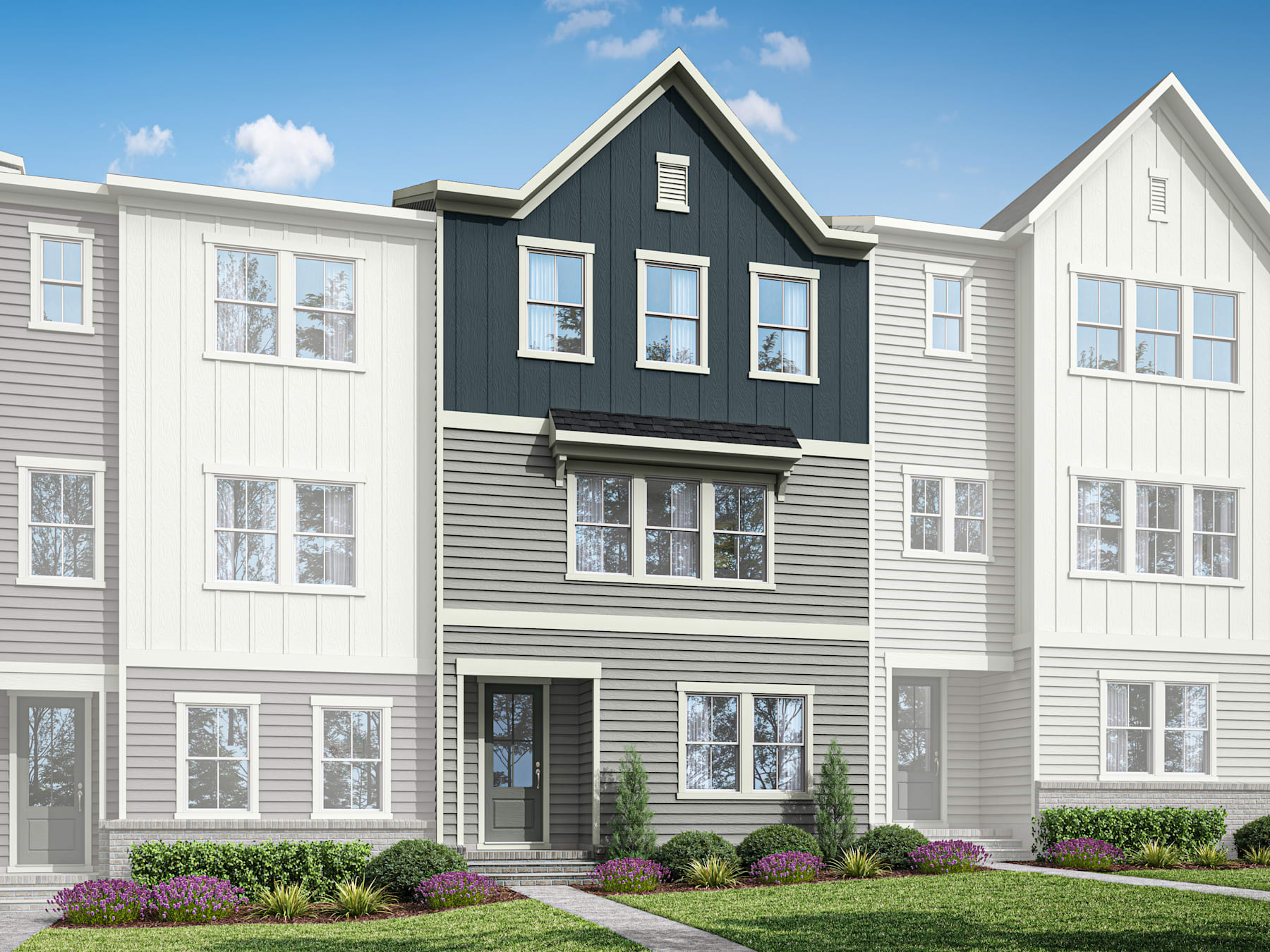 A modern, multi-story townhouse with a gray and white exterior, surrounded by a well-manicured lawn and landscaping, set against a clear blue sky with scattered clouds.