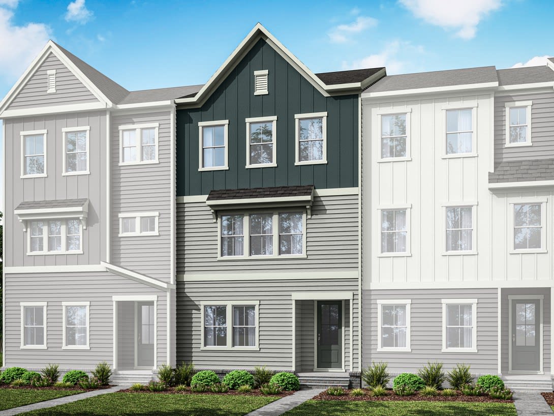 A multi-story townhouse with a gray exterior and white trim, surrounded by landscaped greenery against a clear blue sky.