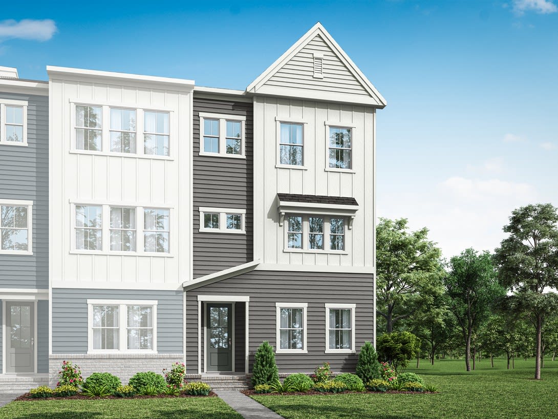 A modern, multi-story townhouse with a gabled roof and a mix of white and gray siding stands in a grassy, tree-lined setting.