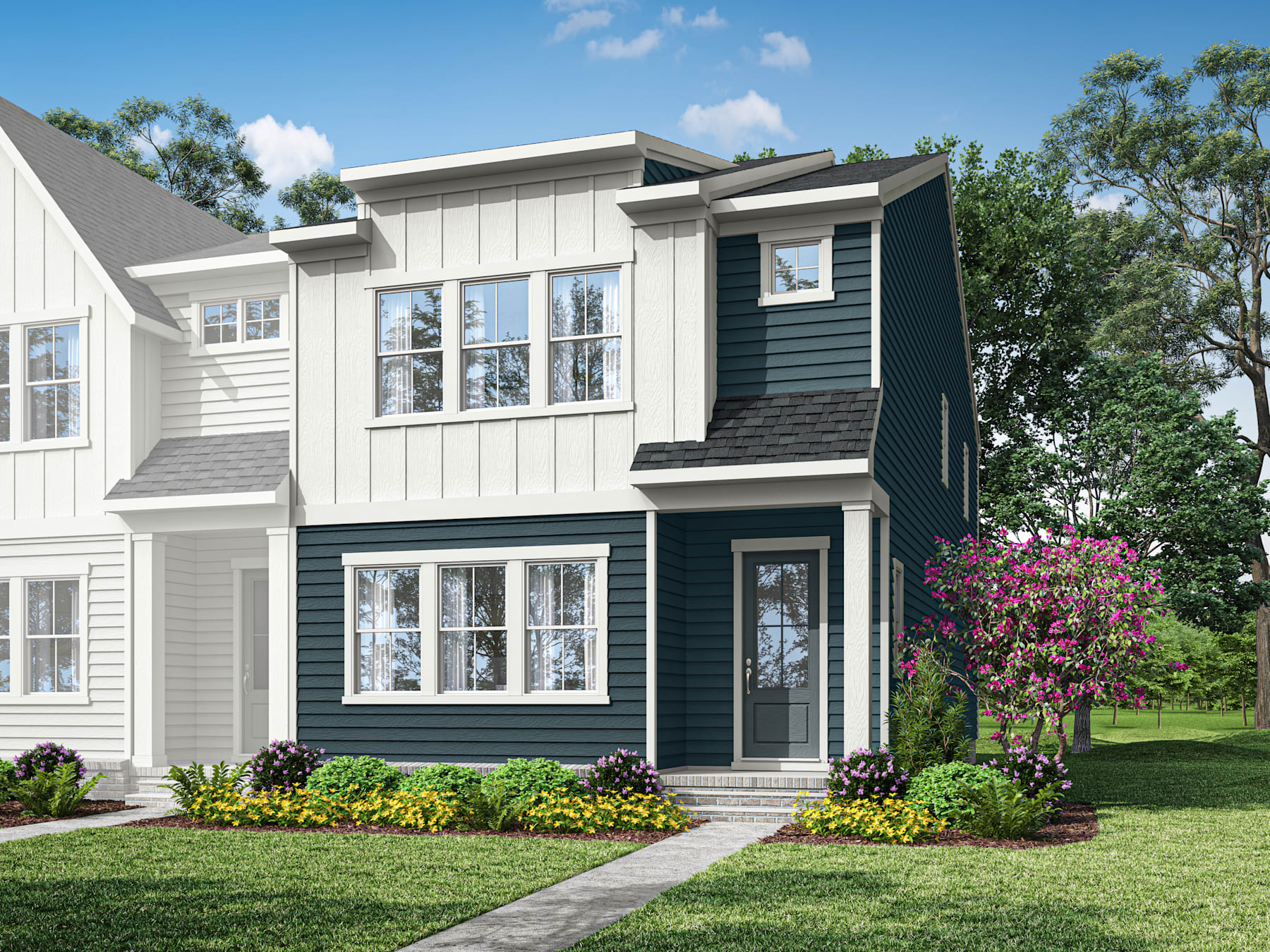 A two-story residential building with a gray exterior, white trim, and a covered porch sits on a well-landscaped property with trees and flowering plants in the foreground.