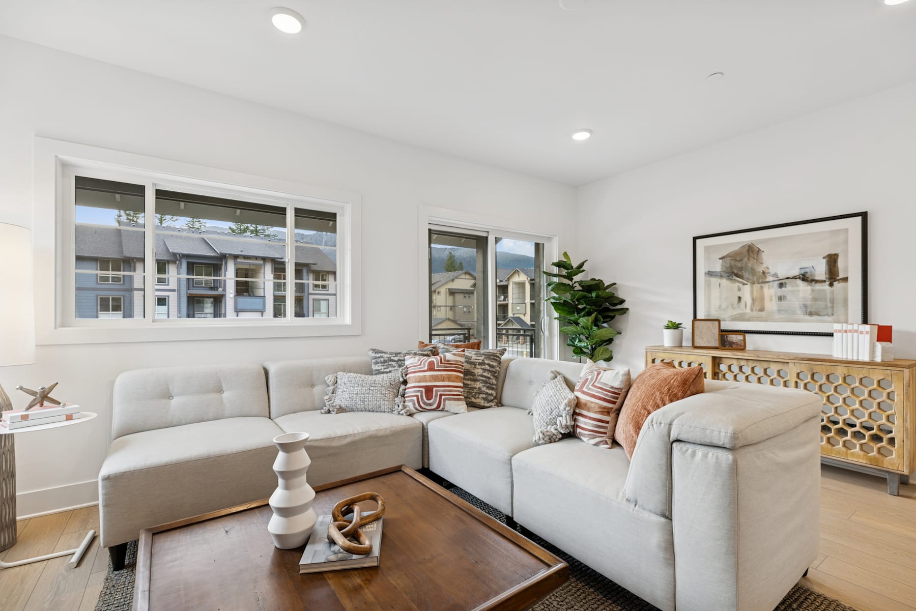 A cozy and inviting living room with plush white sofas, decorative pillows, and a wooden coffee table, set against a backdrop of large windows that allow natural light to flood the space.