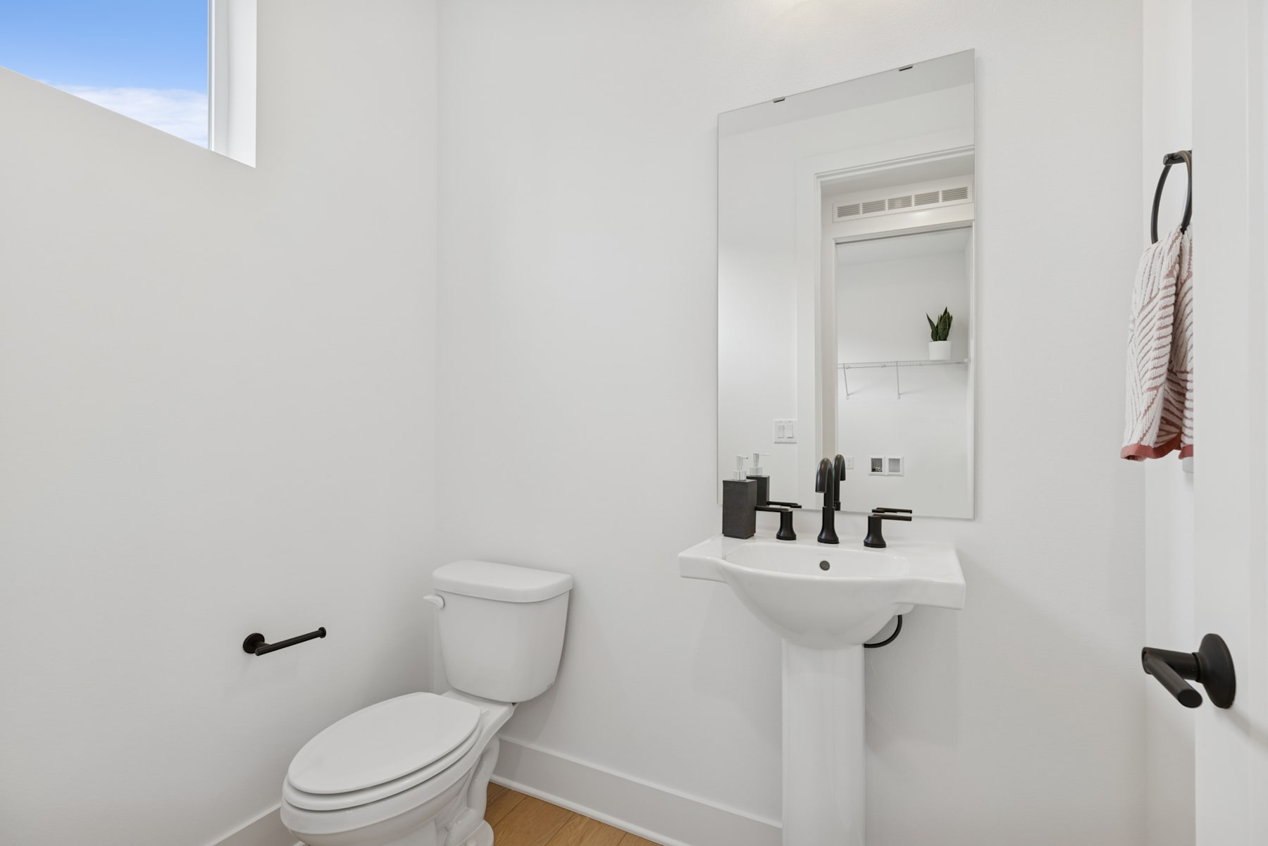A minimalist bathroom with a white toilet, sink, and mirror, set against a plain white wall background.