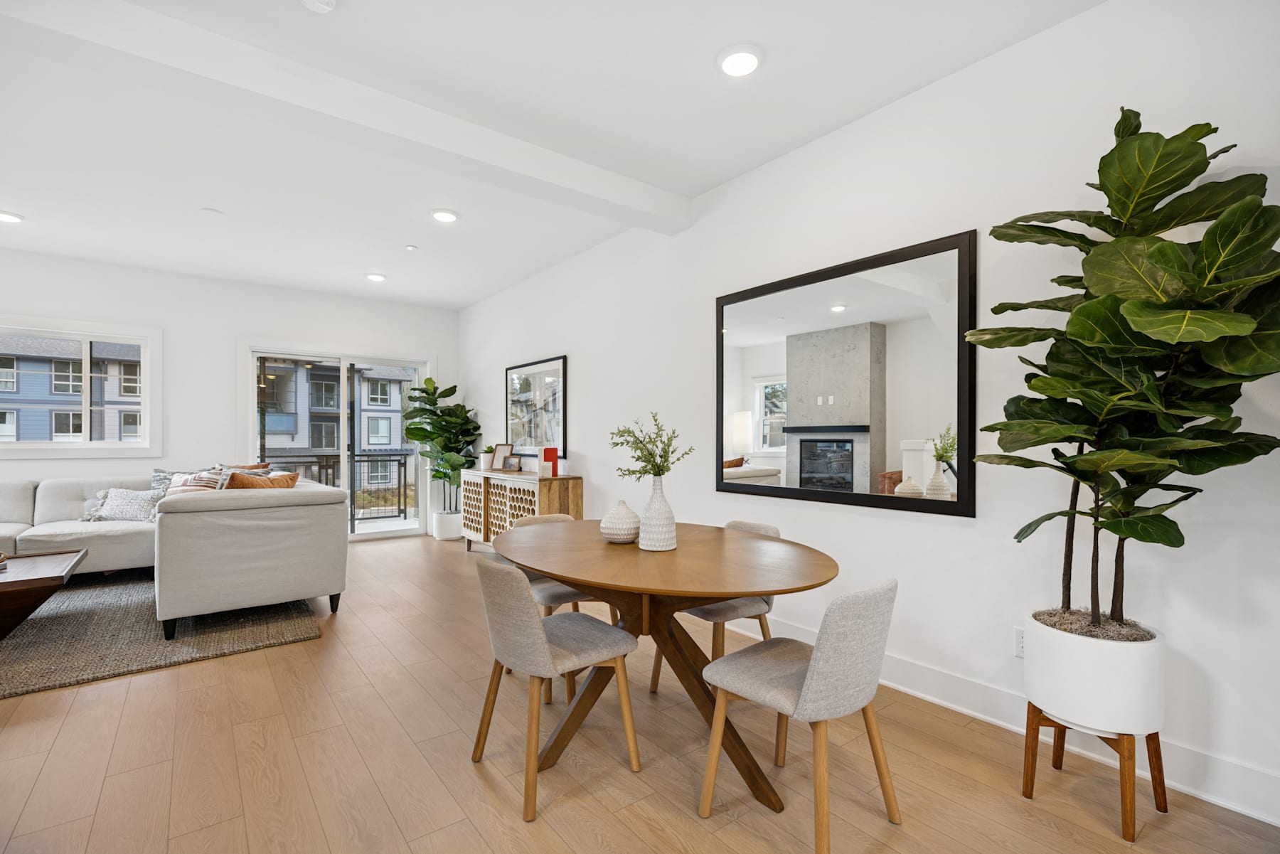 A modern and minimalist dining area with a wooden table and chairs, surrounded by white walls, large windows, and a potted plant, creating a bright and airy atmosphere.