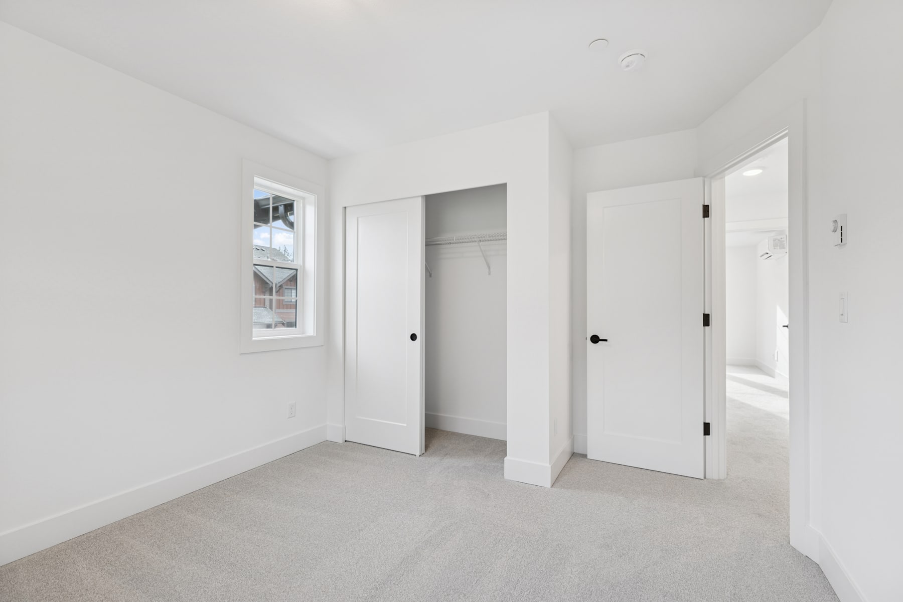 A bright, minimalist room with white walls, a window, and two closed doors, creating a clean and spacious atmosphere.