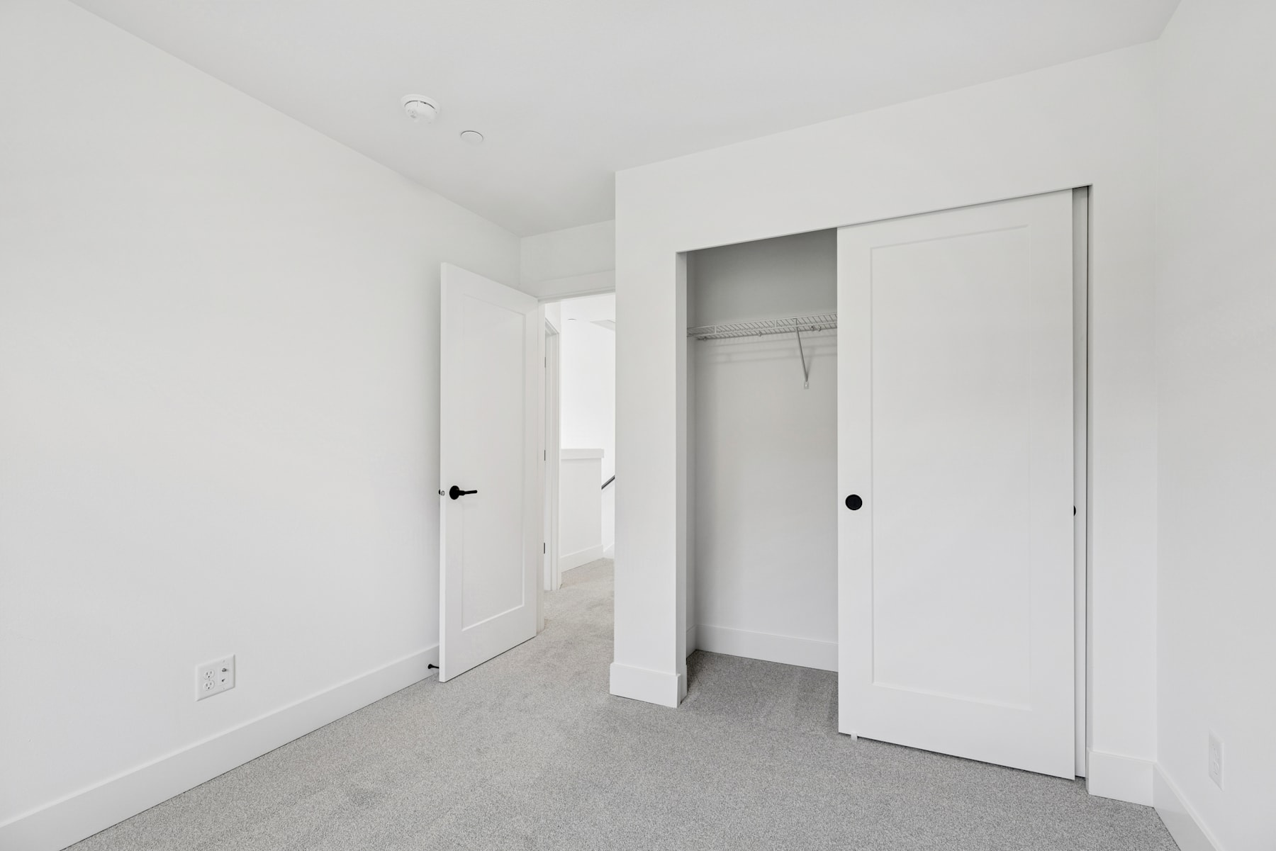 A minimalist, white-walled room with a closet and an open doorway leading to another room.