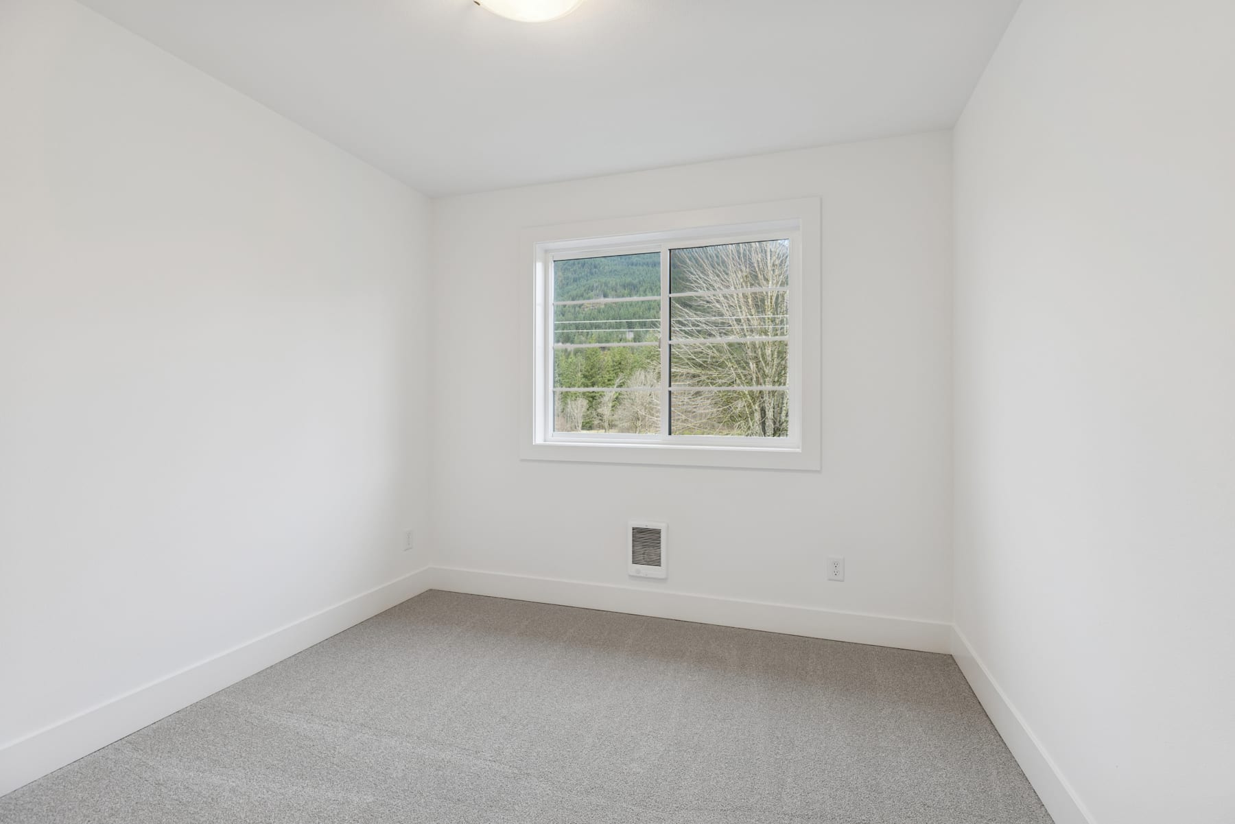 A simple, minimalist room with a large window overlooking a wooded outdoor scene.