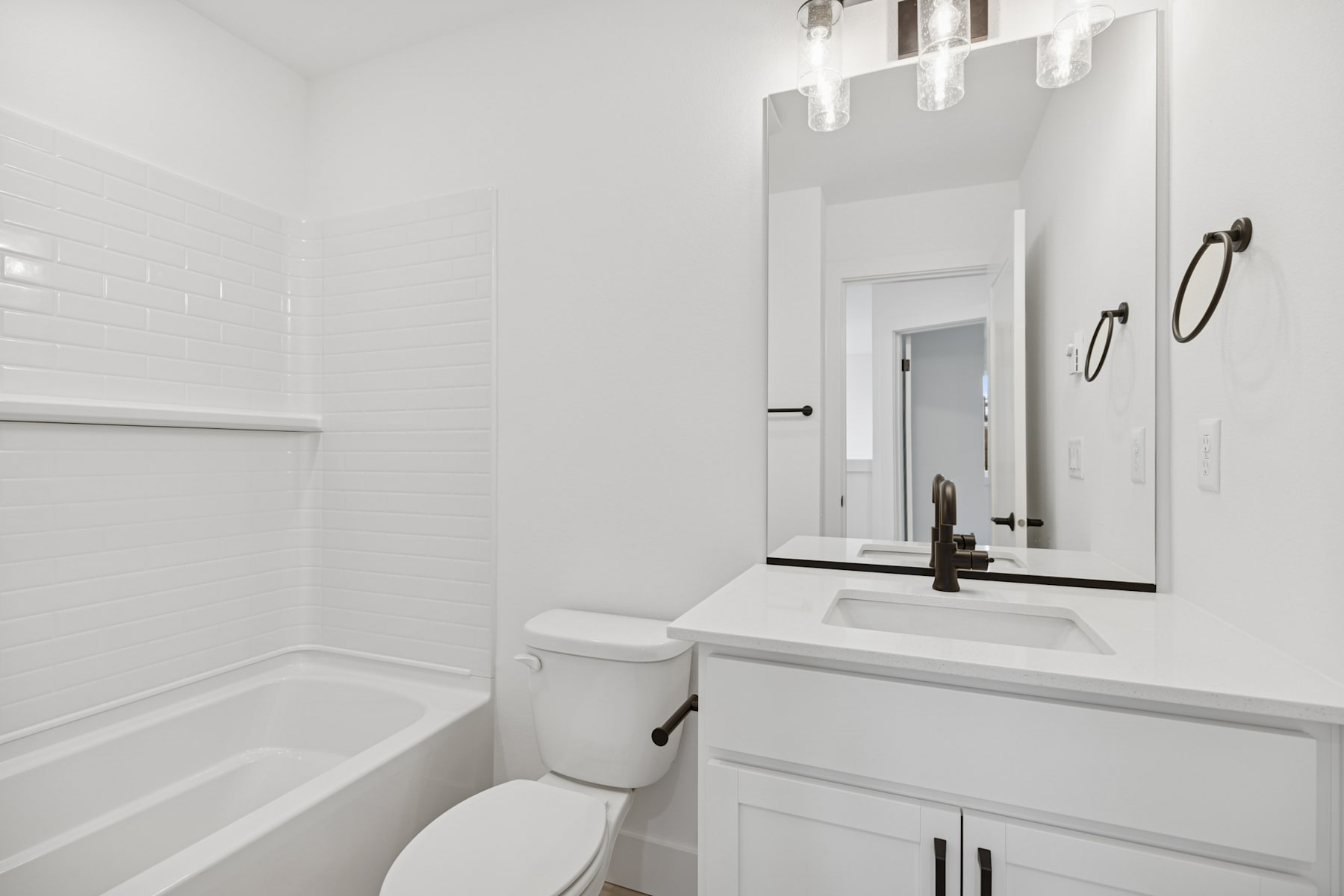 A modern, minimalist bathroom with a white vanity, toilet, and bathtub, illuminated by a sleek light fixture.