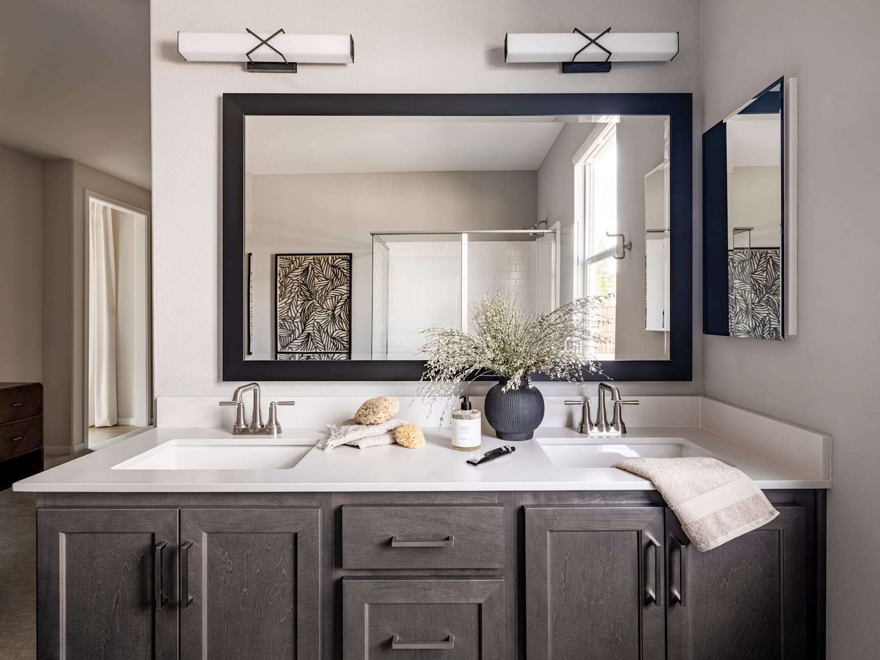A modern and stylish bathroom vanity with a large mirror, white countertop, and decorative accents such as a vase of flowers and towels.