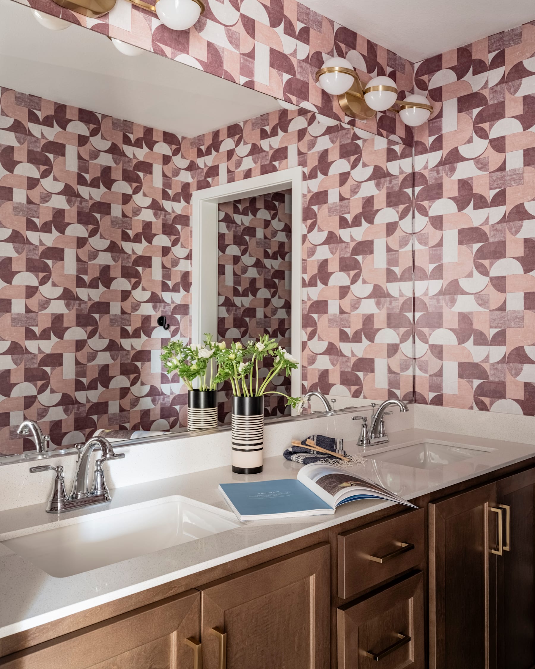 The image depicts a modern bathroom with a patterned tile wall, a double sink vanity with wooden cabinets, and a potted plant on the counter.