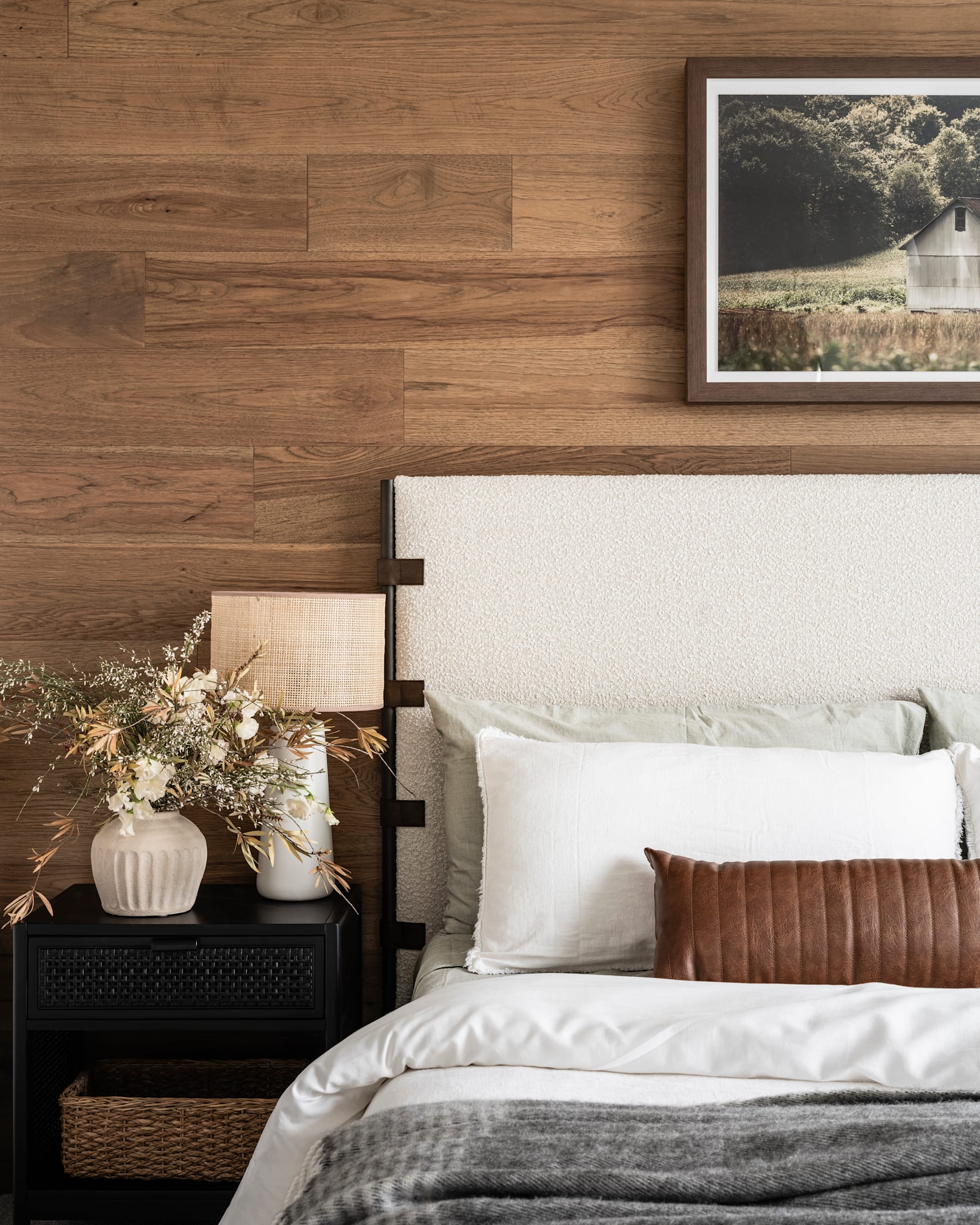 A cozy and inviting bedroom with a wooden accent wall, a white bed with plush bedding, and a framed artwork on the wall, complemented by decorative elements on the nightstand.
