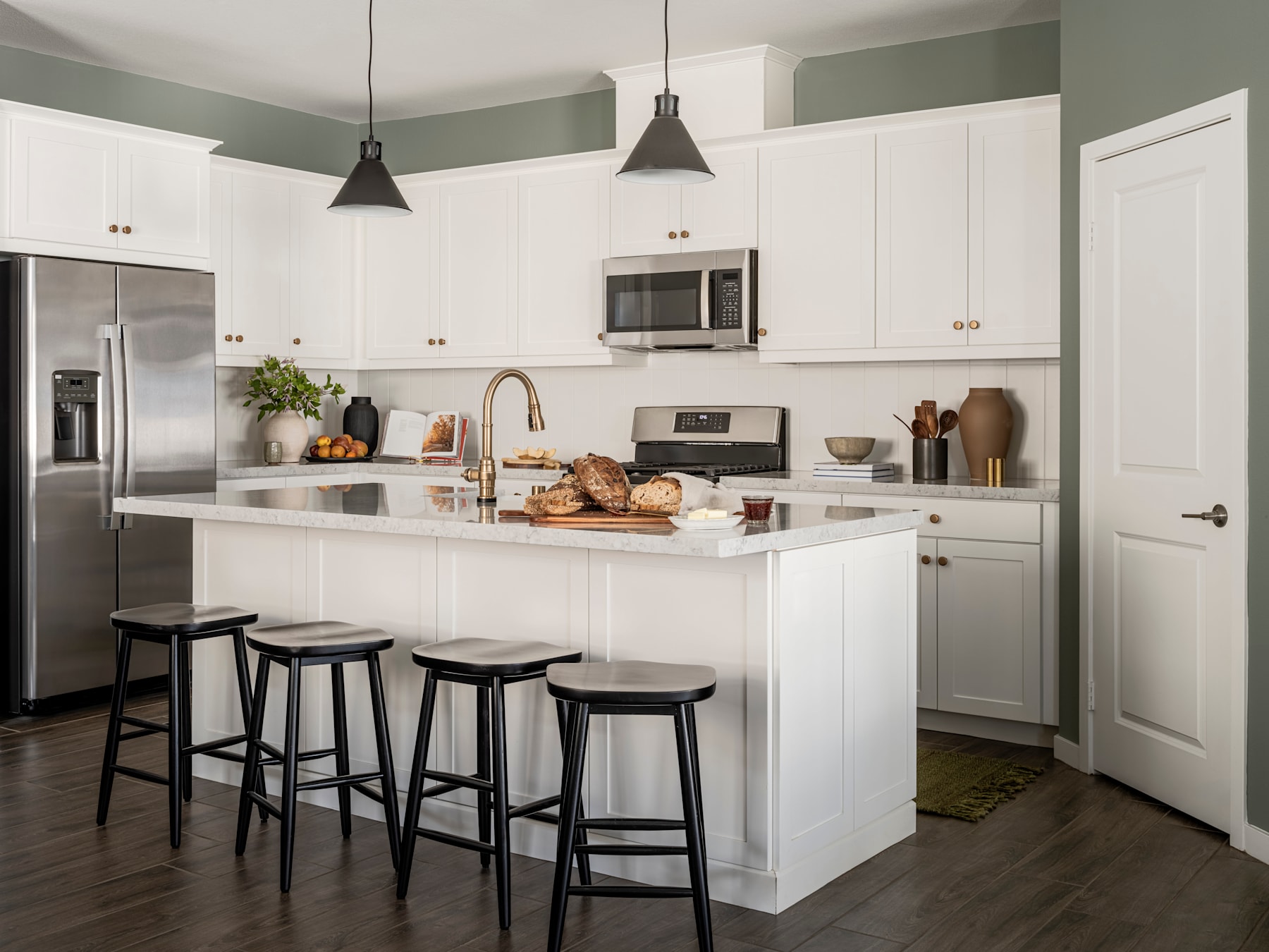 A modern, well-equipped kitchen with white cabinets, stainless steel appliances, and a central island with bar stools, set against a neutral color palette and warm wood flooring.