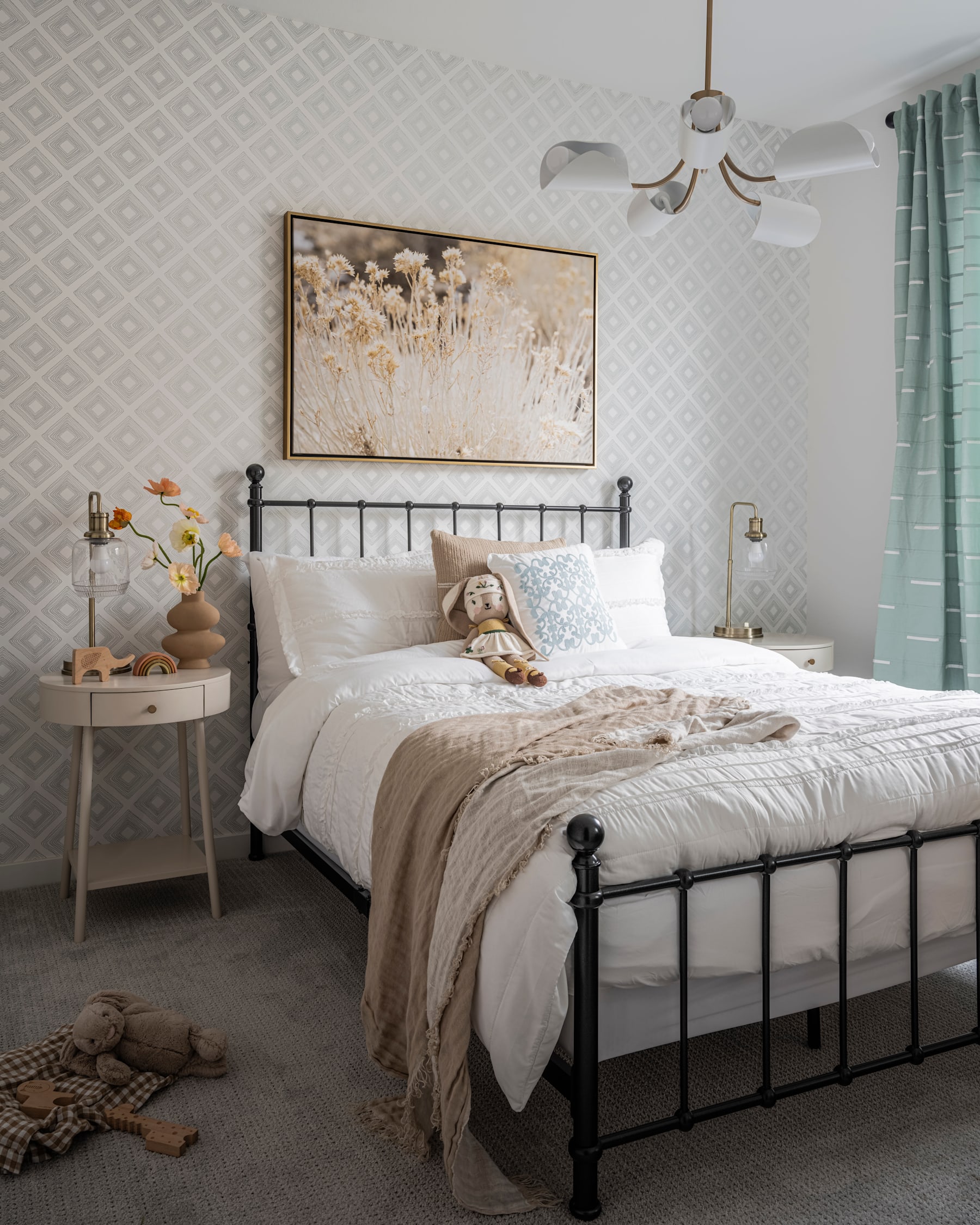 A cozy and inviting bedroom with a metal bed frame, neutral-toned bedding, and a large floral artwork on the wall, complemented by a chandelier and a side table with decorative elements.