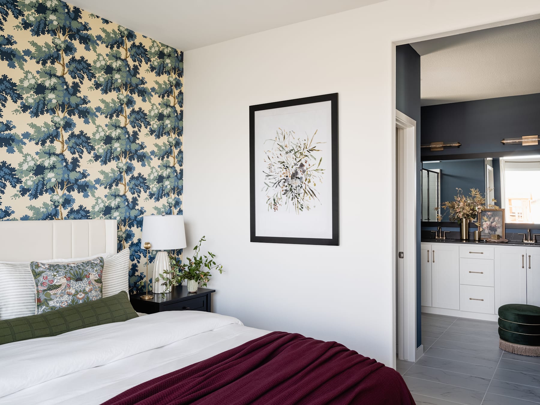 A cozy bedroom with a floral wallpaper accent wall, a framed artwork, and a plush burgundy blanket on the bed.