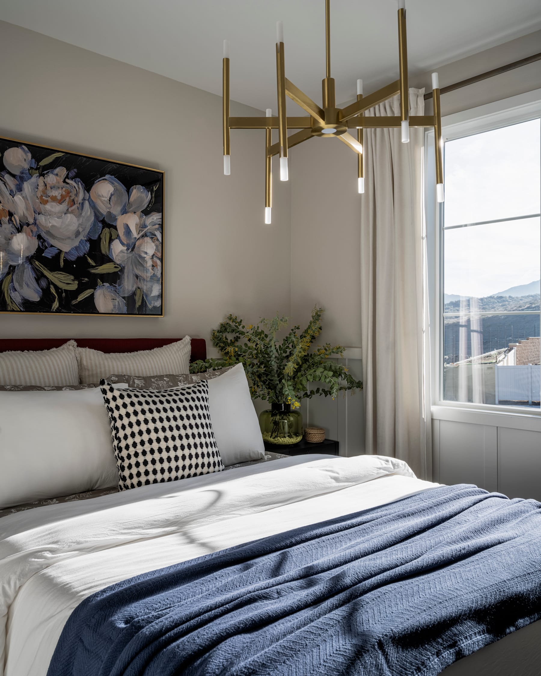 A cozy and stylish bedroom with a large floral artwork, a modern brass chandelier, and a plush bedding arrangement.