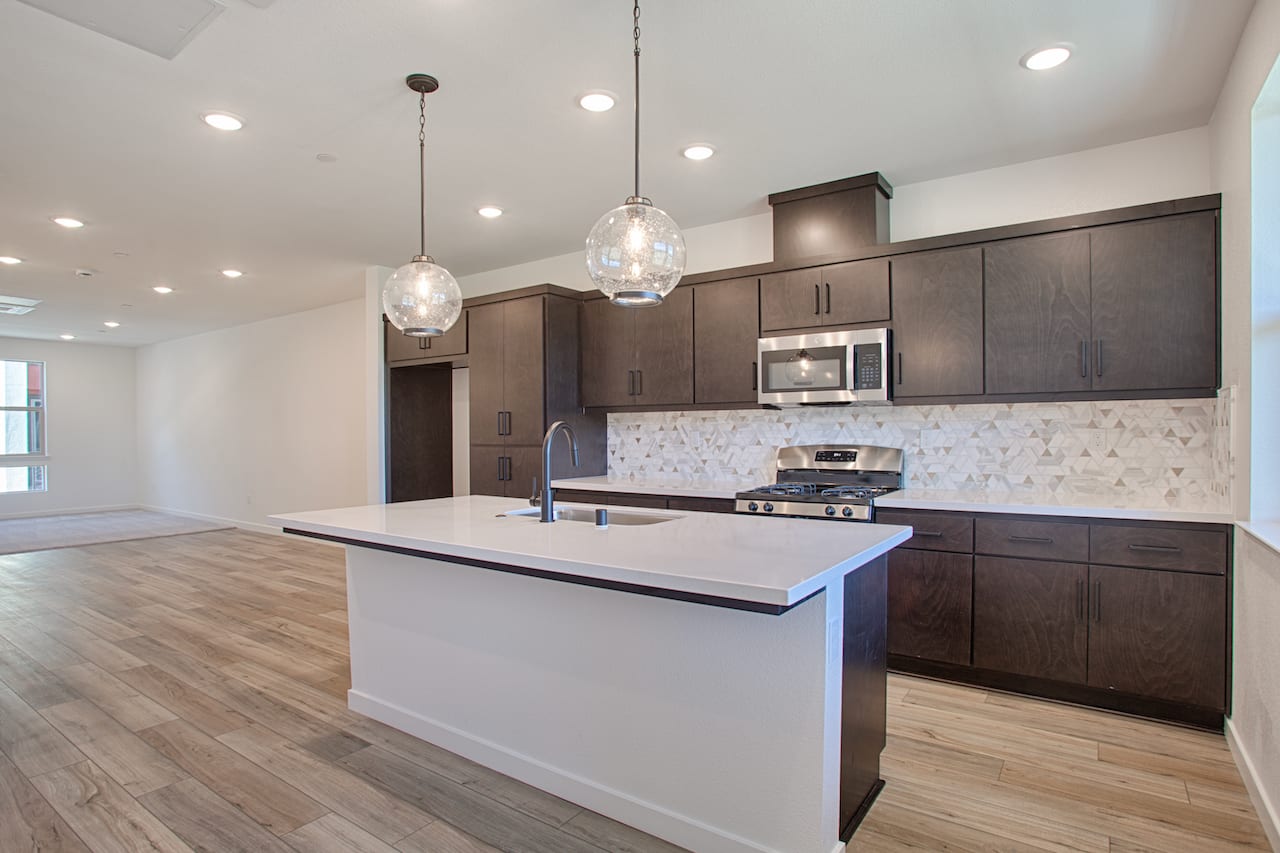 A modern and spacious kitchen with dark wood cabinets, a white island countertop, and pendant lighting fixtures hanging from the ceiling.