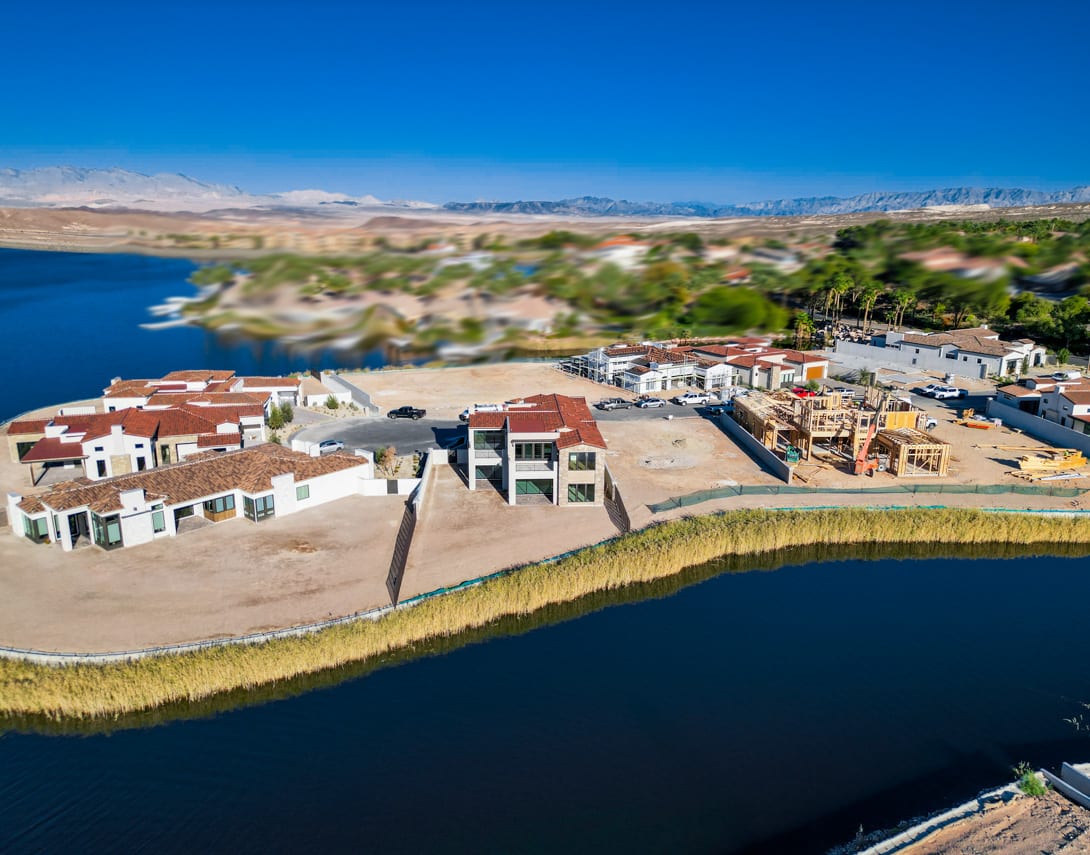 A coastal town nestled along a body of water, with colorful buildings and structures in the foreground and a mountainous landscape in the background under a clear blue sky.