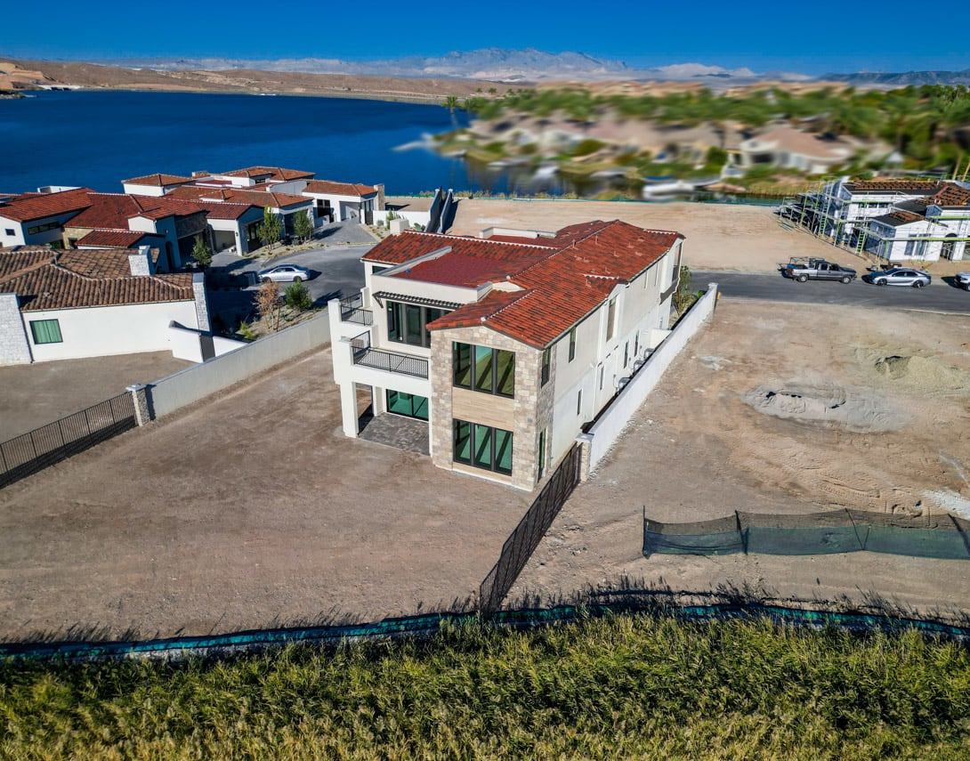A coastal town with red-roofed buildings nestled among lush greenery, overlooking a vast, serene body of water under a clear blue sky.