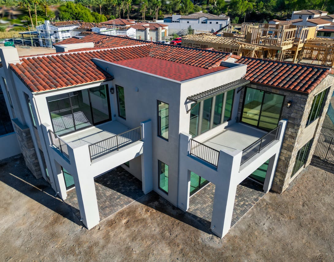 The image shows a group of modern, multi-story residential buildings with red tile roofs, surrounded by lush greenery in the background.