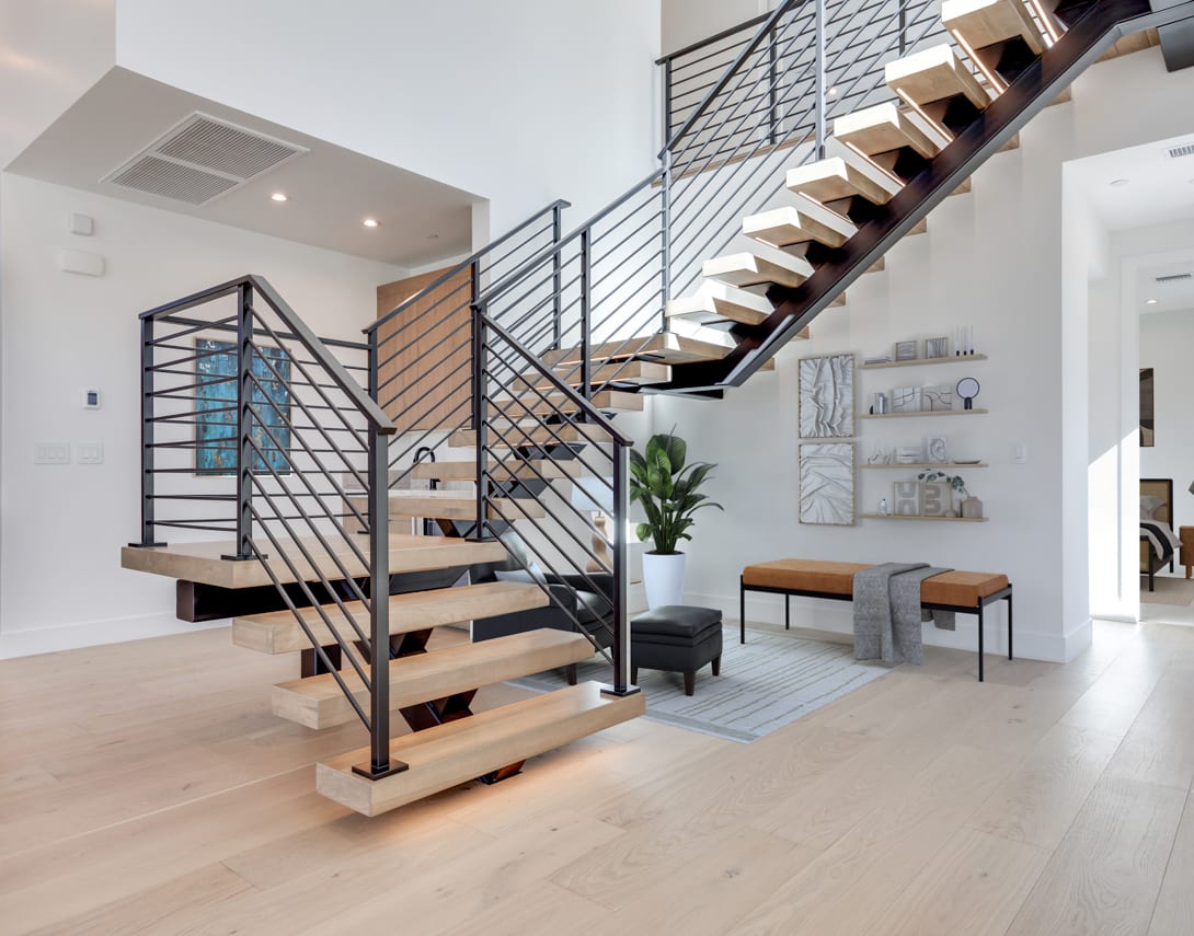 A modern, open-concept interior with a sleek, metal staircase leading up to a second level, surrounded by minimalist decor and furnishings.