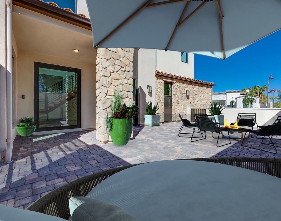 A cozy outdoor patio with stone walls, a large umbrella, and comfortable seating arrangements, set against a backdrop of a clear blue sky.