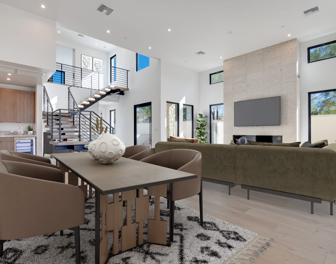 A modern and open-concept living space with a dining area, comfortable seating, and a staircase leading to an upper level, surrounded by large windows that allow natural light to flood the room.