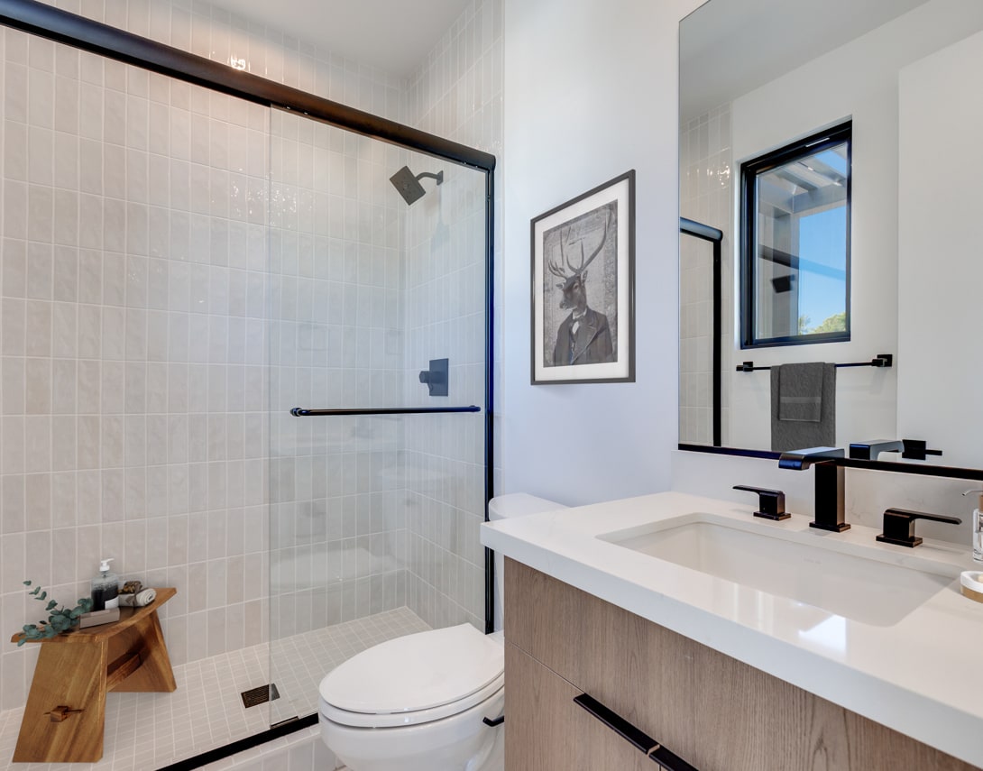 A modern bathroom with a glass shower enclosure, a white vanity with a sink, and a framed artwork on the wall.