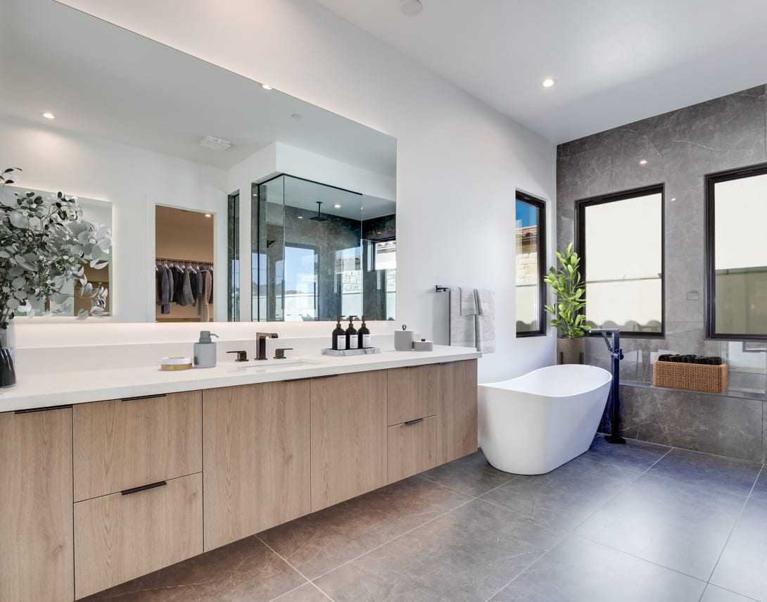 A modern and spacious bathroom with a freestanding bathtub, a vanity with a double sink, and a large mirror. The room features a minimalist design with neutral colors and natural materials.
