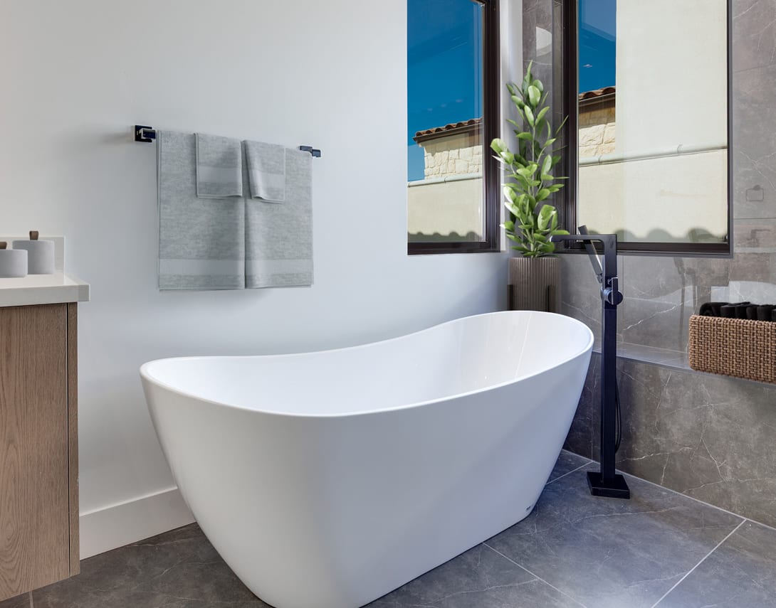 A modern, minimalist bathroom with a freestanding white bathtub, a wooden vanity, and a large window overlooking a lush plant.