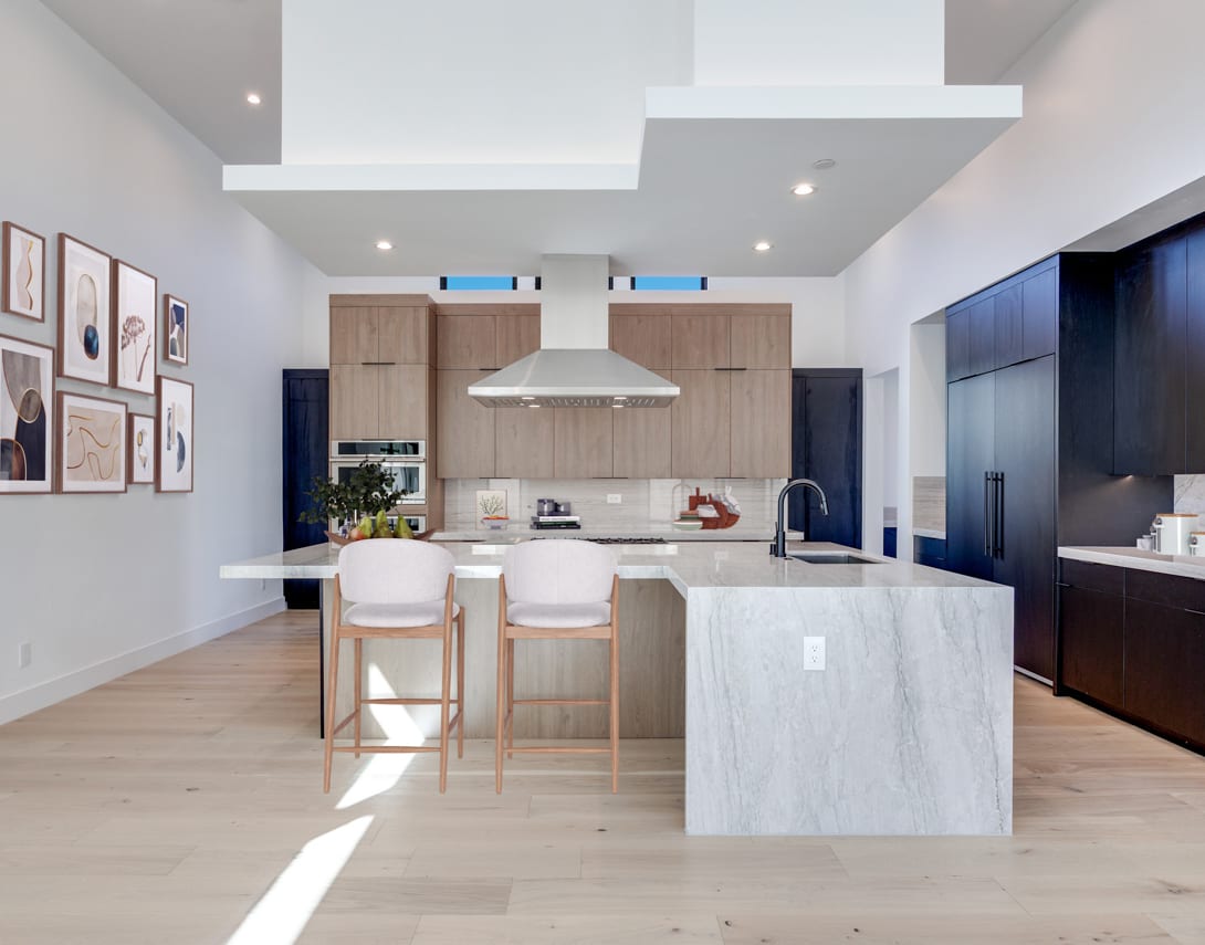 A modern, open-concept kitchen with a white marble island, wooden cabinets, and a sleek range hood, surrounded by framed artwork on the walls.