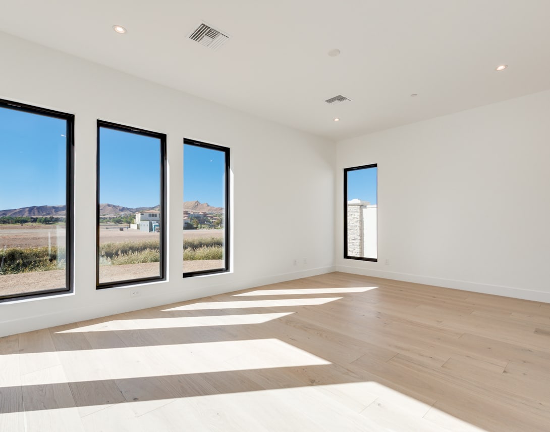 A spacious, well-lit room with large windows offering a scenic view of the surrounding landscape, featuring a hardwood floor and a minimalist design.