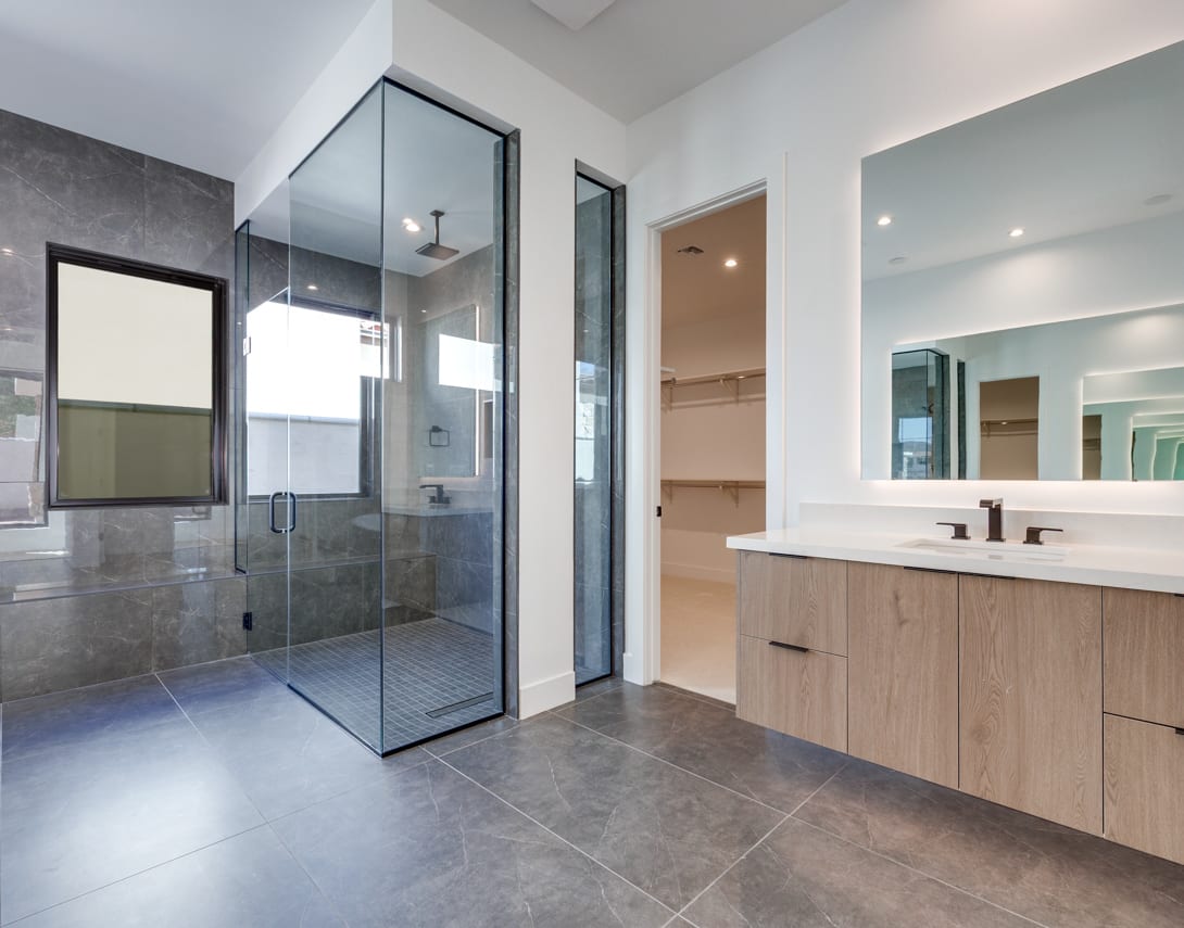A modern and spacious bathroom with a glass-enclosed shower, a vanity with a white countertop, and a tiled floor.