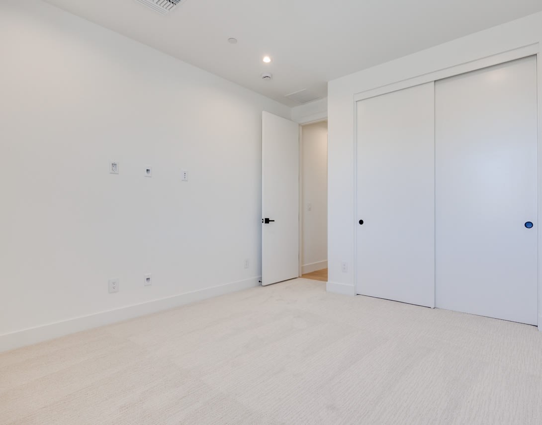 A minimalist, white-walled room with a hardwood floor and two closed doors, one of which appears to be a closet.