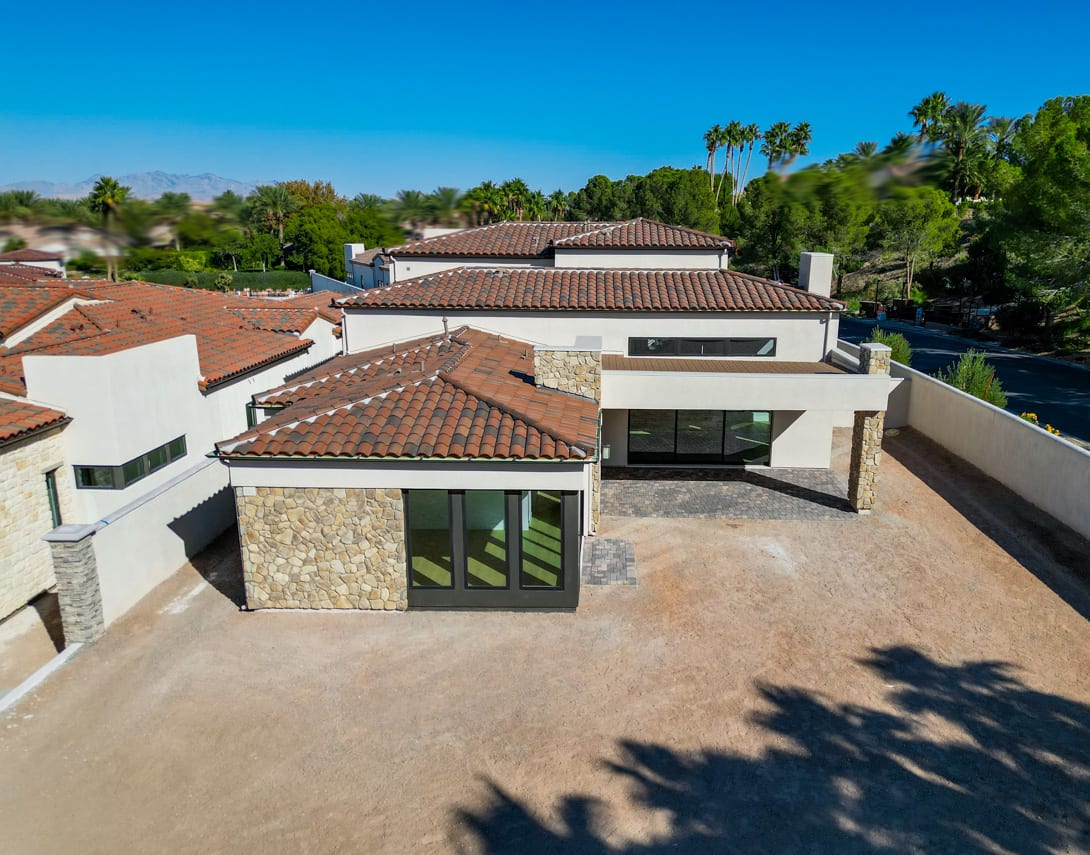 A residential neighborhood with a collection of Mediterranean-style homes with red tile roofs, surrounded by lush greenery and a clear blue sky.