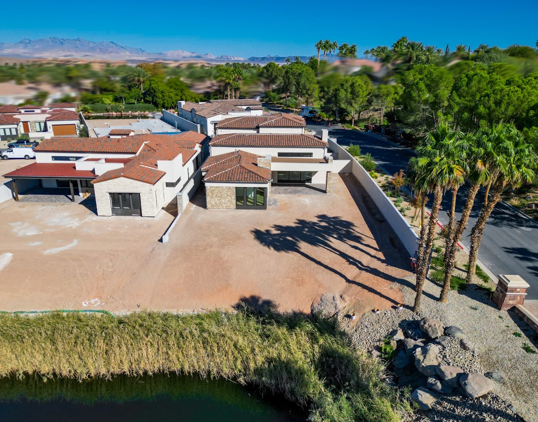 A residential neighborhood with red-tiled roofs nestled among lush palm trees, set against a backdrop of mountains and a clear blue sky.