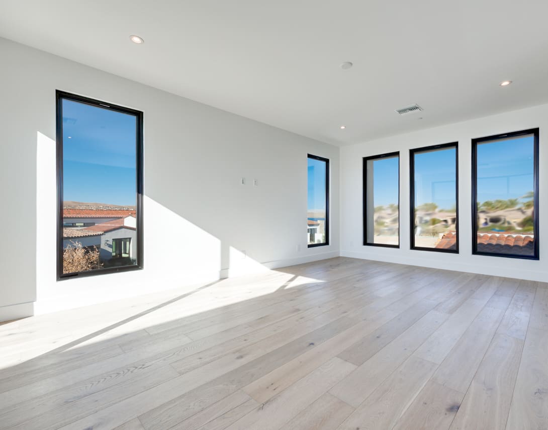 A spacious, modern room with large windows offering a scenic view of the surrounding landscape, featuring a hardwood floor and a minimalist design.