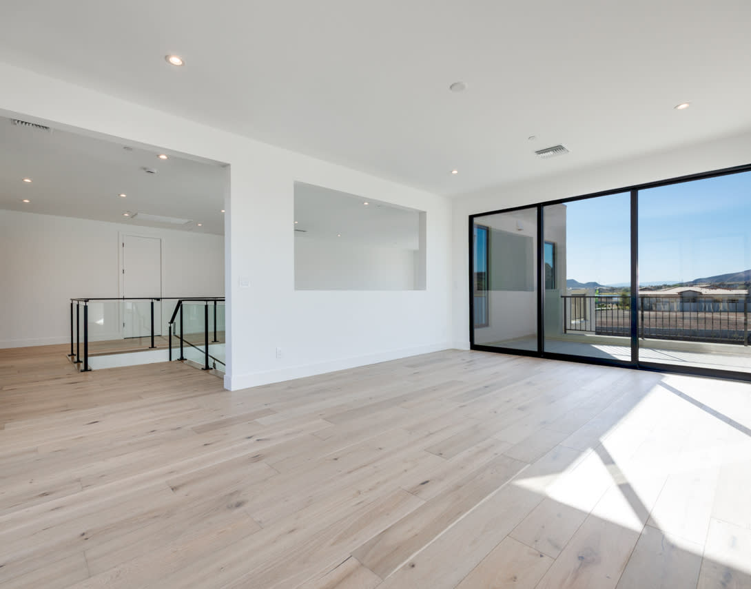 A spacious, modern living room with large windows overlooking a scenic outdoor view, featuring a hardwood floor and minimalist design.