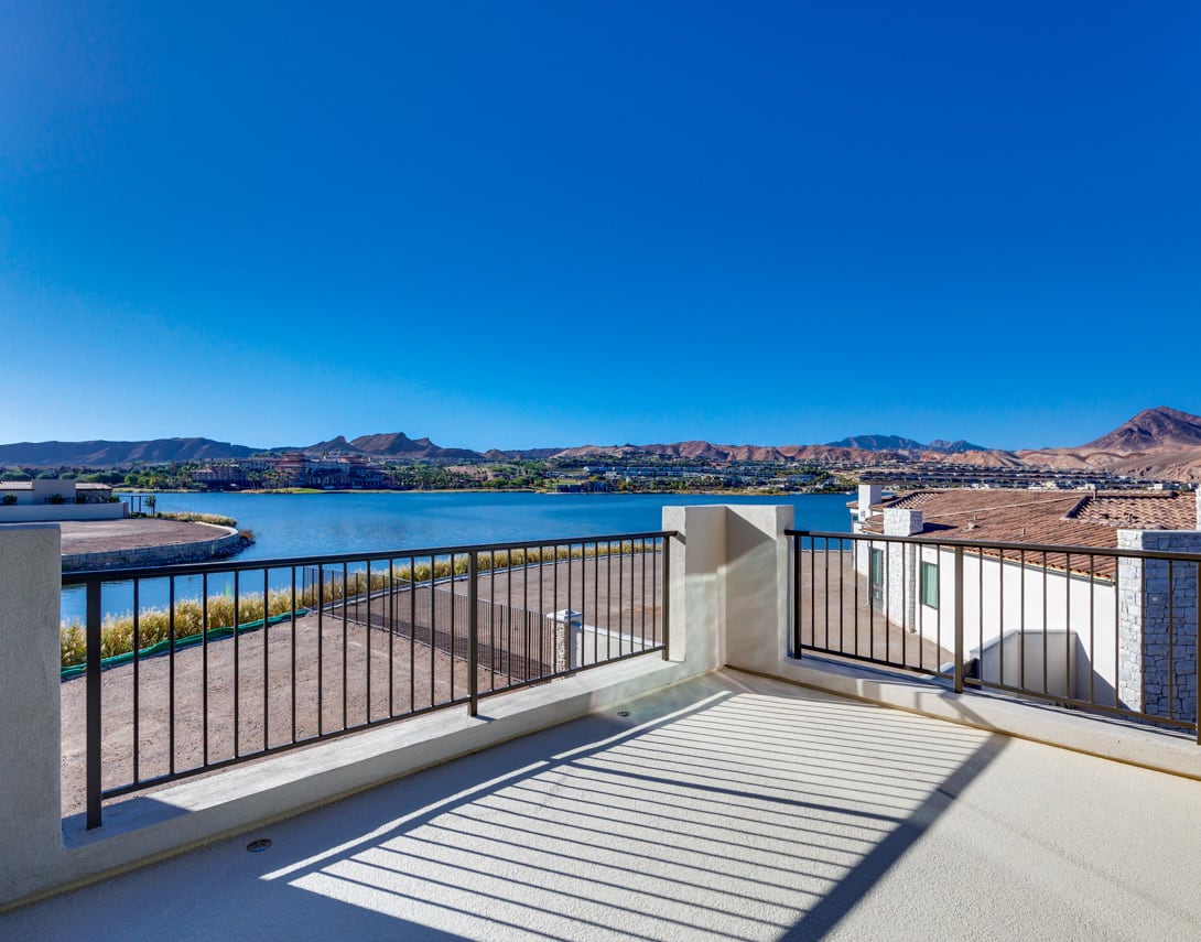 A balcony overlooking a scenic waterfront with mountains in the distance, under a clear blue sky.