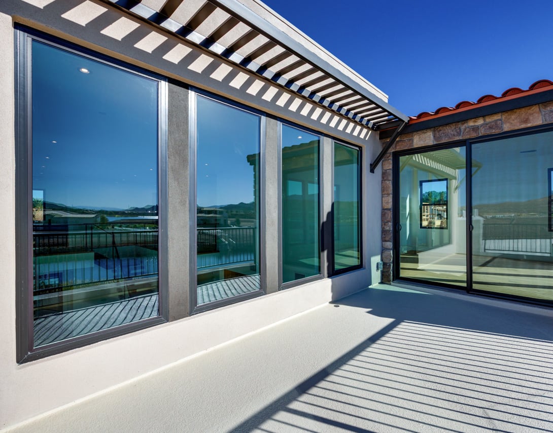 A modern, glass-enclosed patio or balcony with a wooden deck and a view of the surrounding landscape in the background.