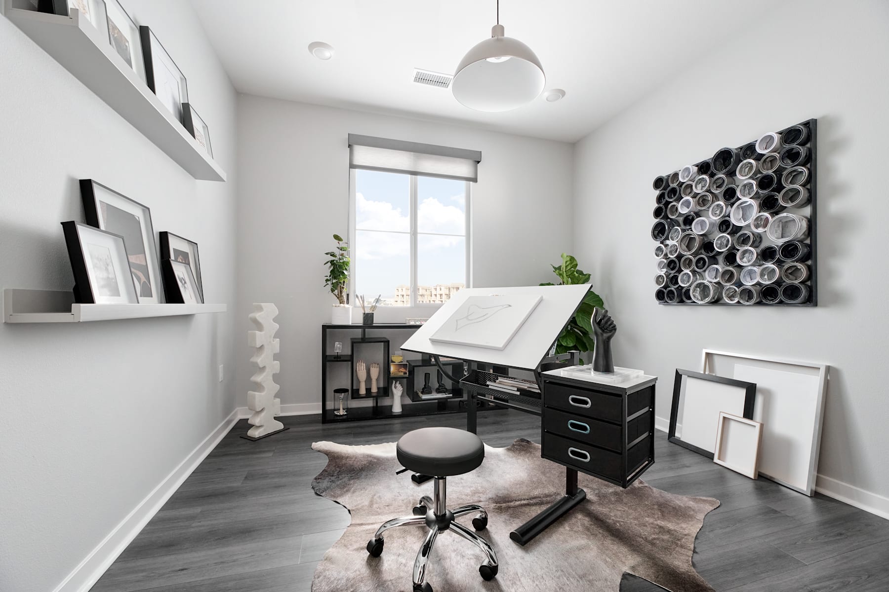 A modern, minimalist home office space with a white desk, black and white artwork, and a cozy sheepskin rug on the hardwood floor.