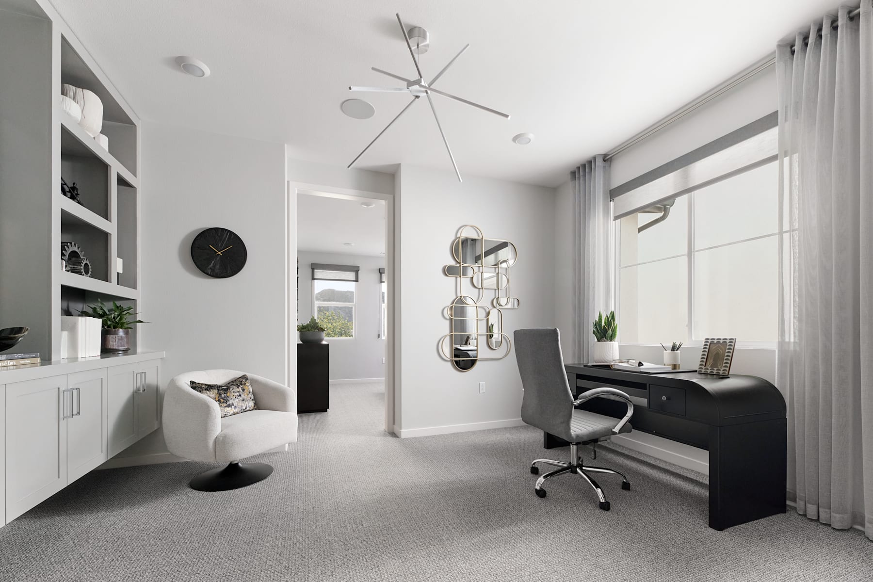 A modern, minimalist home office space with white walls, a black desk, and various decorative elements such as a ceiling fan, wall clocks, and potted plants.