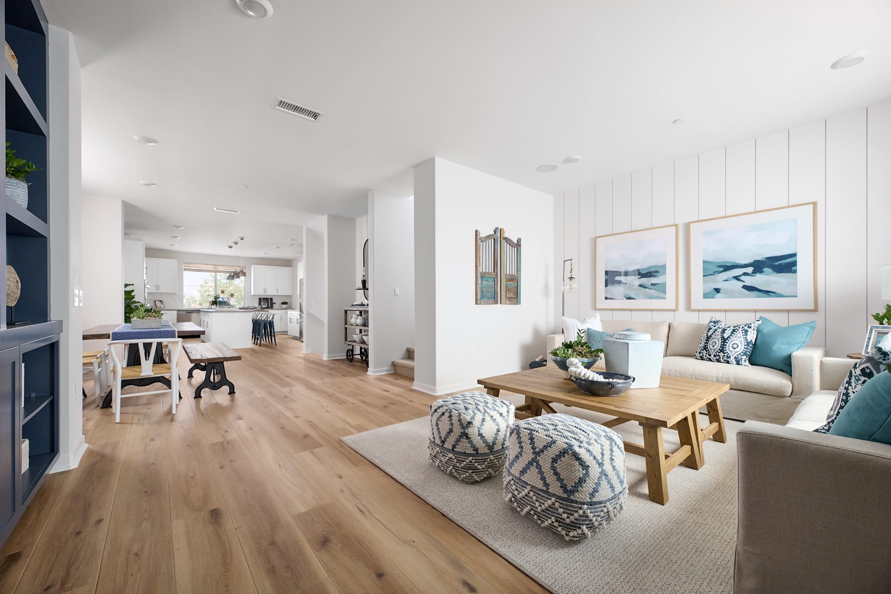A bright and airy open-concept living space with a cozy seating area, wooden dining table, and a glimpse of the kitchen in the background.